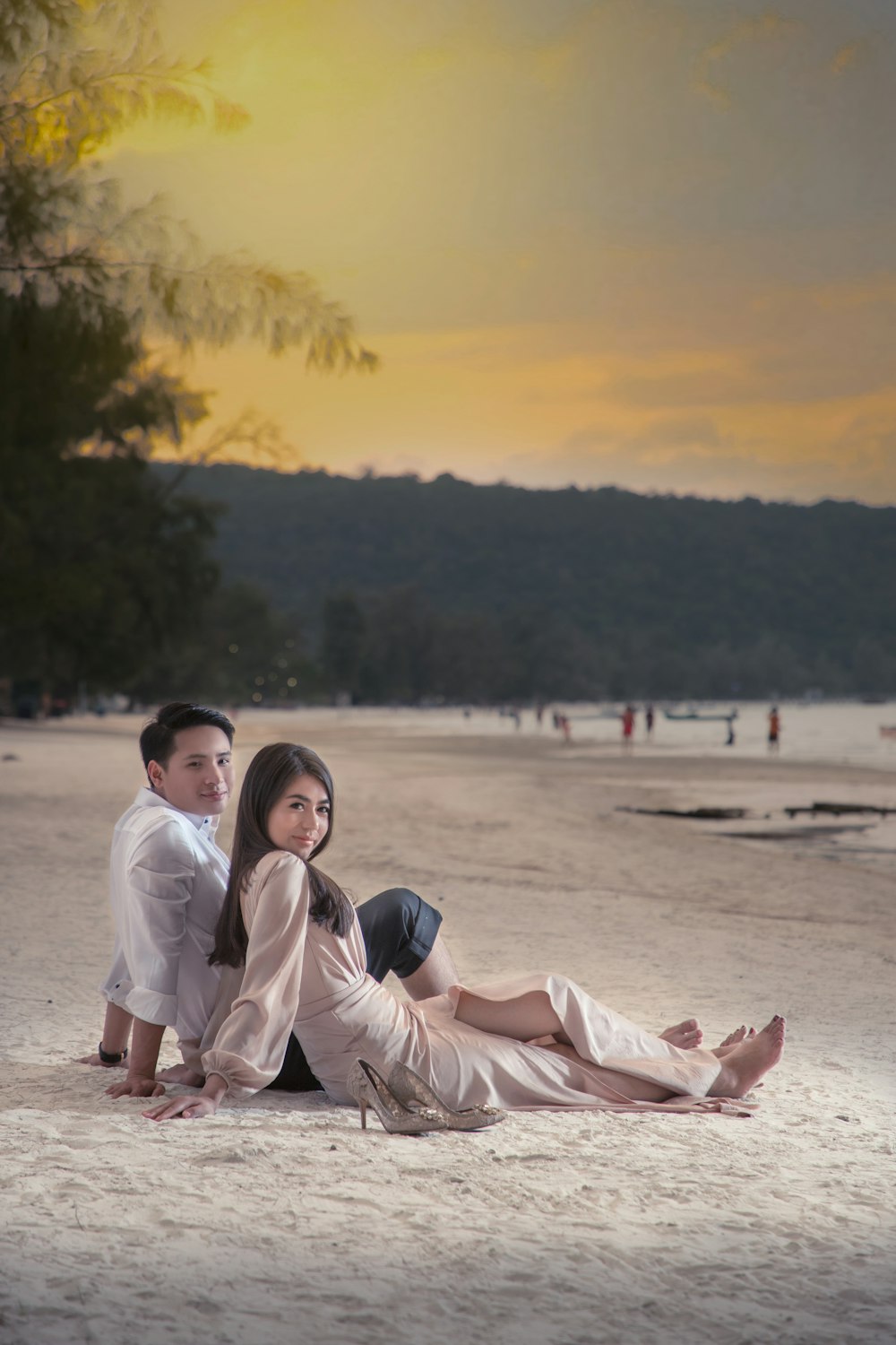 man and woman sitting on sand during sunset