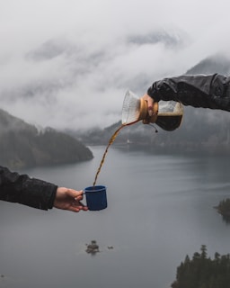 person pouring coffee to the another person's cup near body of water