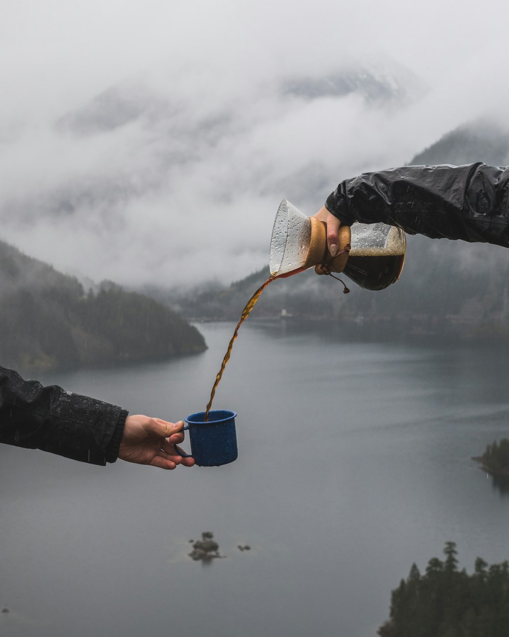 une personne qui verse du café dans la tasse d’une autre personne près d’un plan d’eau ;