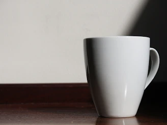 Minimalist ceramic mugs with soft shadows, placed on a smooth wooden countertop.