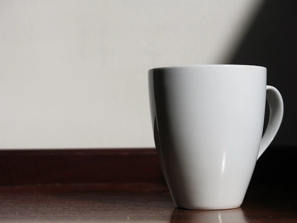 Minimalist ceramic mugs with soft shadows, placed on a smooth wooden countertop.