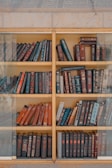 A closed wooden bookshelf with glass doors showcasing neatly arranged novels and decor.