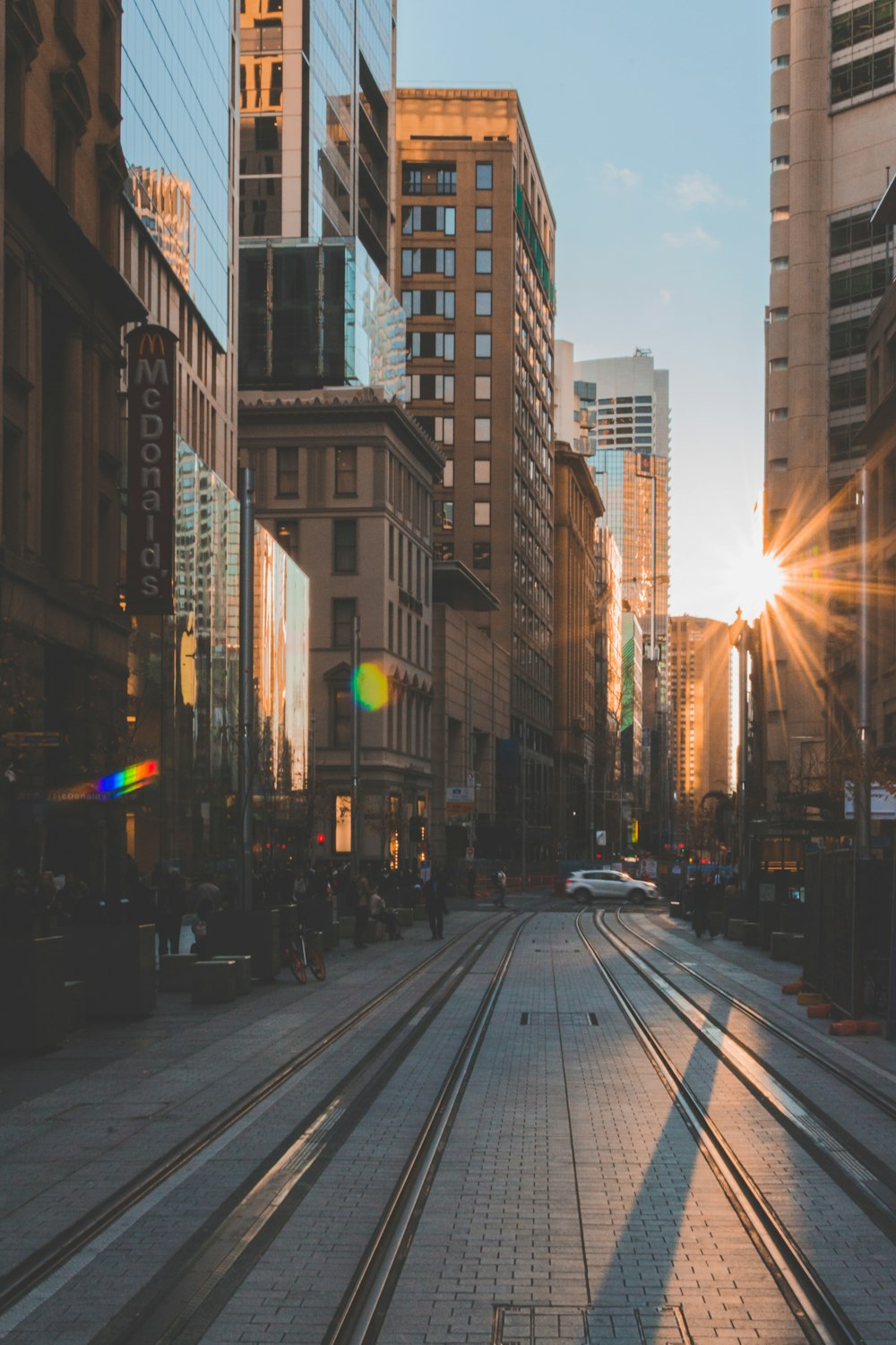 Menschen, die am Straßenrand zwischen Gebäuden mit Sonnenlicht gehen