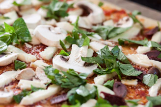 Close-up of fresh vegetables and cheese being prepared for pizza toppings in a rustic kitchen.