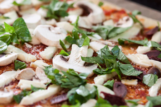 Close-up of fresh vegetables and cheese being prepared for pizza toppings in a rustic kitchen.