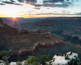 A scenic view of the Grand Canyon at sunset with a small group of tourists listening to a guide.