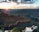 A breathtaking view of the Grand Canyon at sunset with the sun casting a warm glow over the vast, rugged landscape. The canyon's layers are highlighted by the sunlight, creating a dramatic contrast with the shadows. A group of people is sitting on a rocky ledge in the foreground, possibly enjoying the peaceful scene.