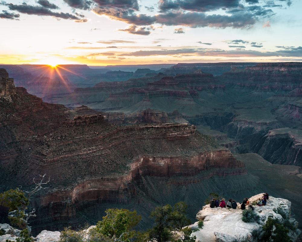 aerial view of people sitting on cliff near mountain during golden hour