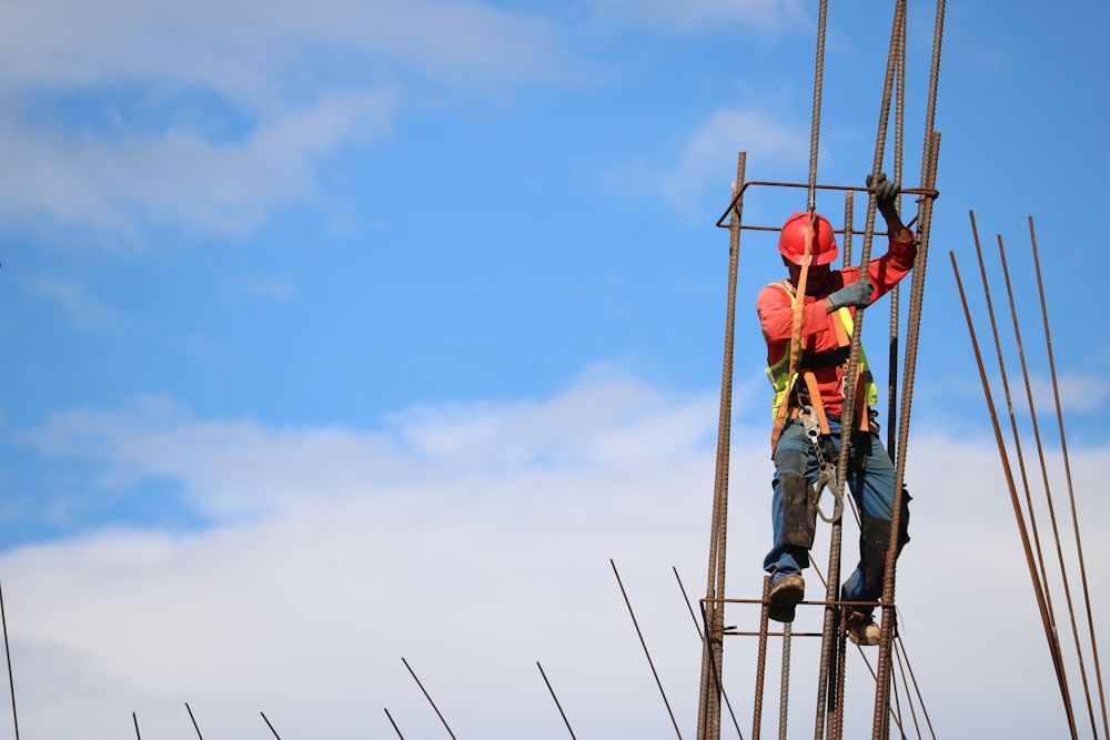 homme portant un casque de sécurité rouge pendu à une barre d’armature brune