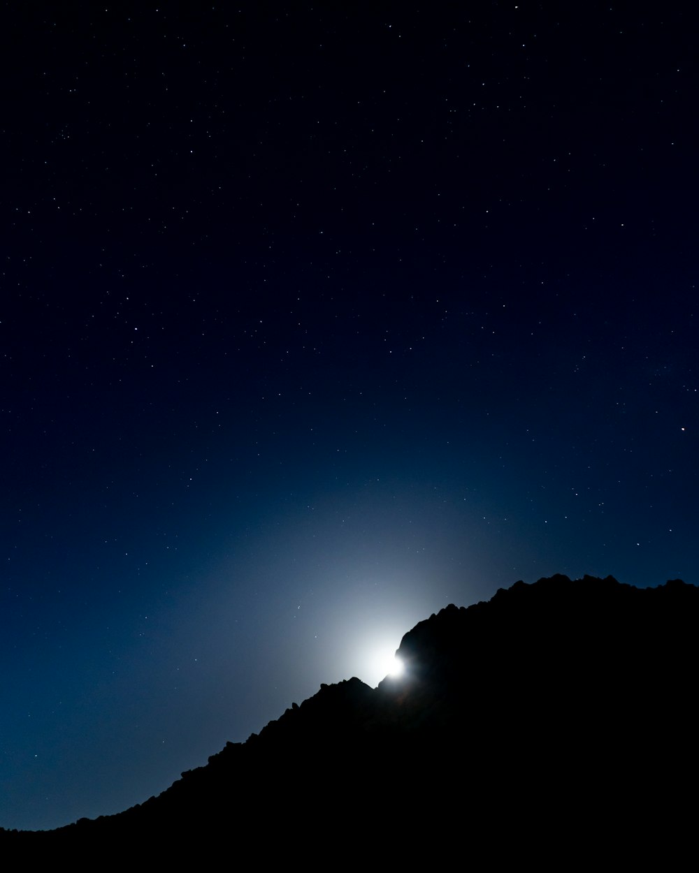 Uma luz brilhante brilha no céu noturno acima de uma montanha