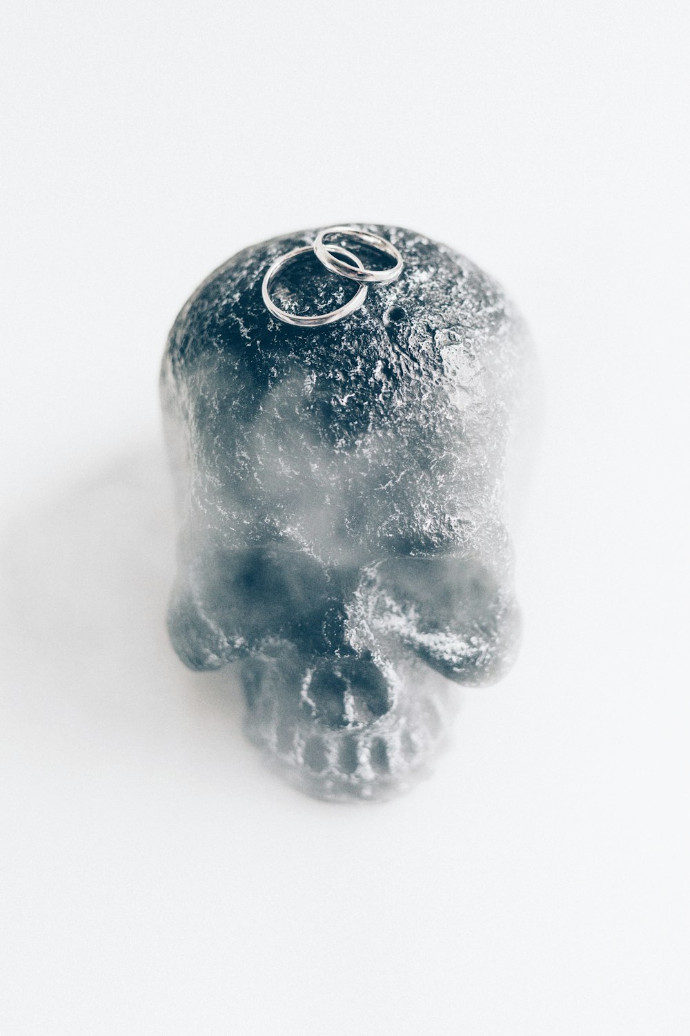two silver-colored wedding rings on gray skull