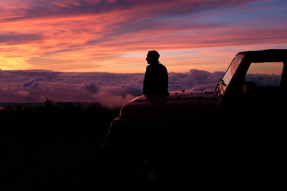 Uomo seduto sul cofano dell'auto che guarda i cieli sotto l'ora d'oro