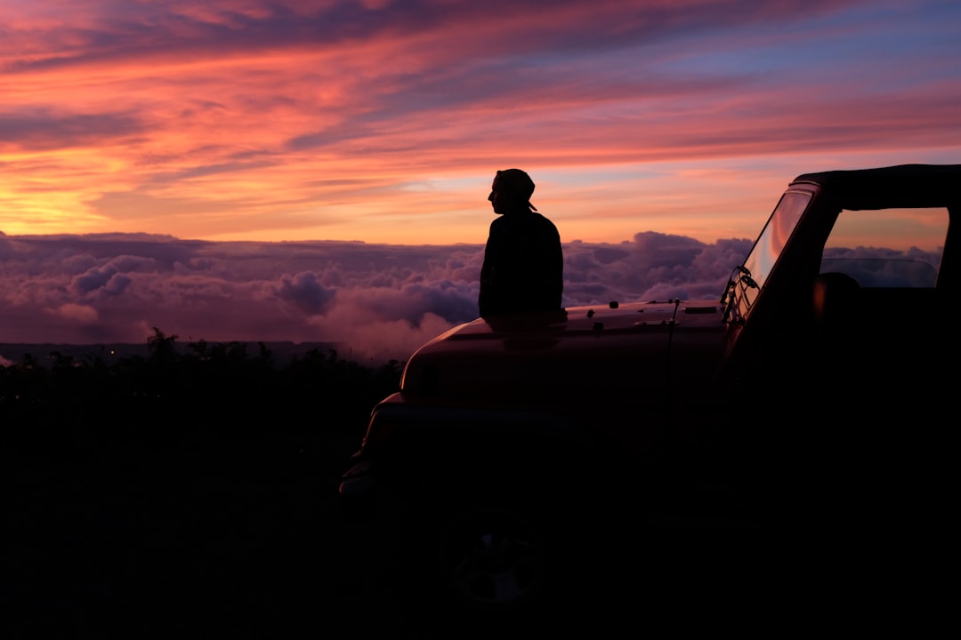 man sitting on car hood watching the skies under golden hour,