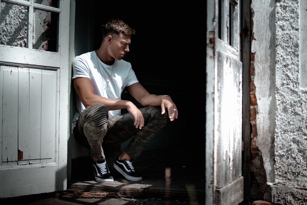 man in white crew-neck T-shirt sitting beside white door