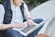 man using MacBook while sitting on bench