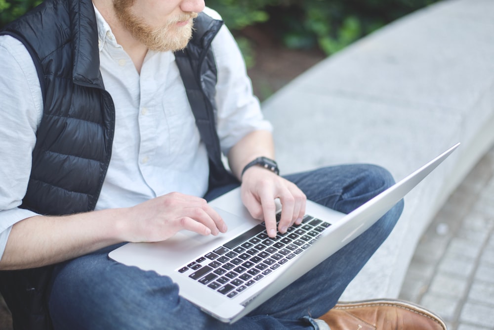 man using MacBook while sitting on bench