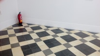 A room corner features a black and white checkered floor with a fire extinguisher placed against the white walls.