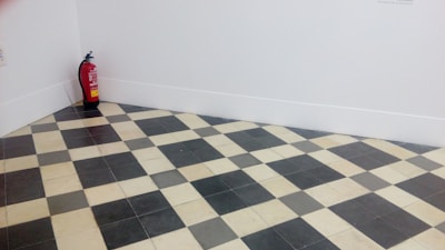 A room corner features a black and white checkered floor with a fire extinguisher placed against the white walls.