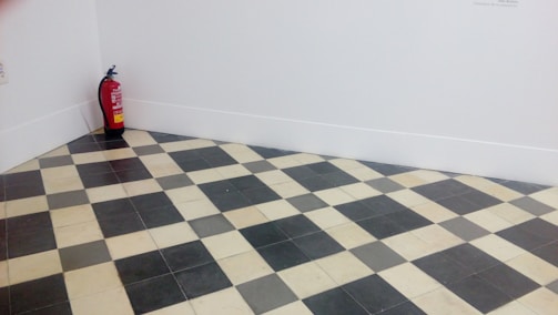 A room corner features a black and white checkered floor with a fire extinguisher placed against the white walls.