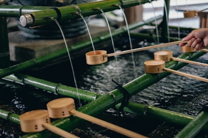 A traditional Japanese water purification basin made from bamboo, with water trickling down from above into a stone basin. Several wooden ladles are placed over the bamboo, typically used for ritual cleansing.
