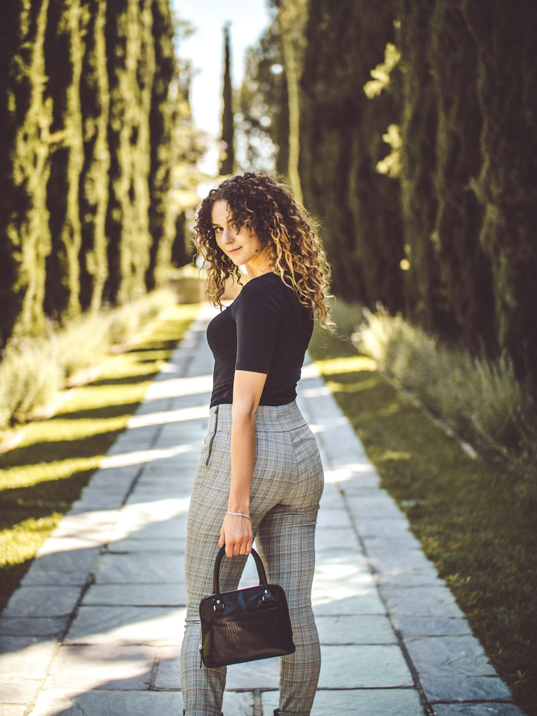 woman standing on pathway between pine trees