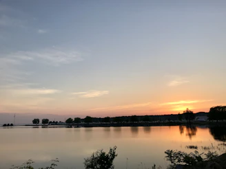 A soft orange and pink sunset reflecting off a calm lake surface surrounded by trees.