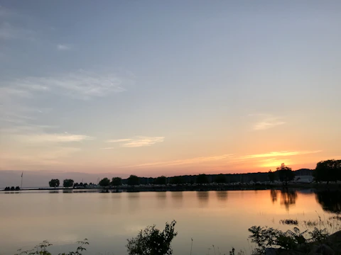 A soft orange and pink sunset reflecting off a calm lake surface surrounded by trees.