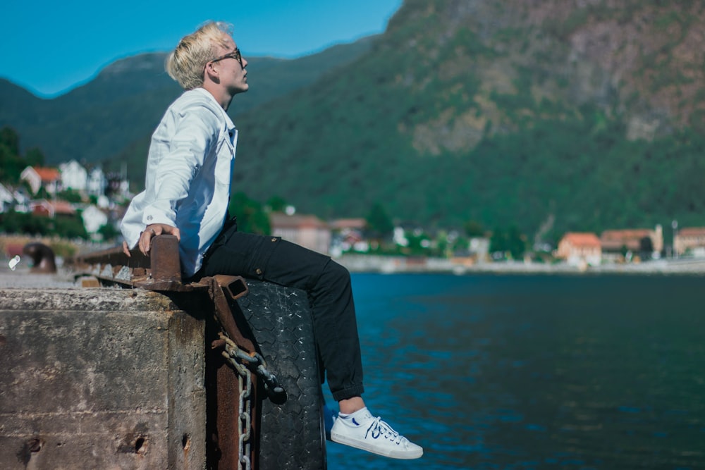 man sitting at the edge of the dock during day