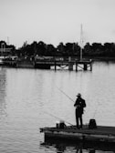 A scenic view of a dock with fishing gear and a phone resting on the railing.