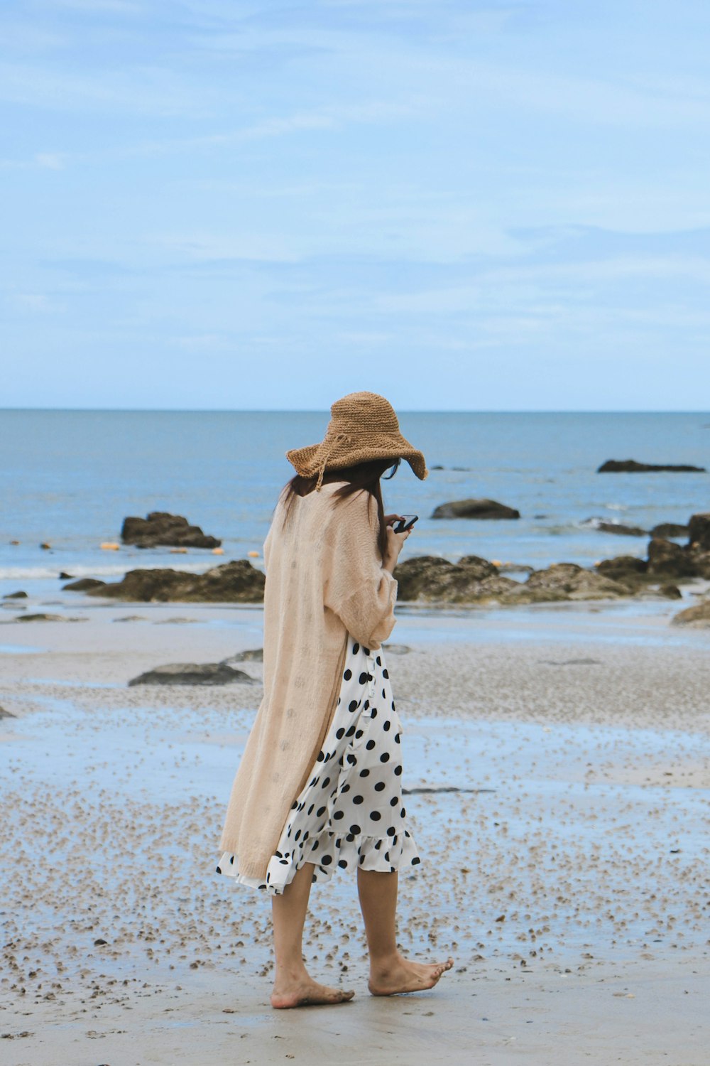 woman wearing sun hat walking along seashore