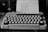 A vintage typewriter on a wooden desk with a fresh sheet of paper ready for typing.