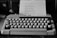 A vintage typewriter on a wooden desk with a fresh sheet of paper ready for typing.