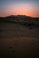 Sunrise over endless sand dunes with footprints leading toward the horizon.