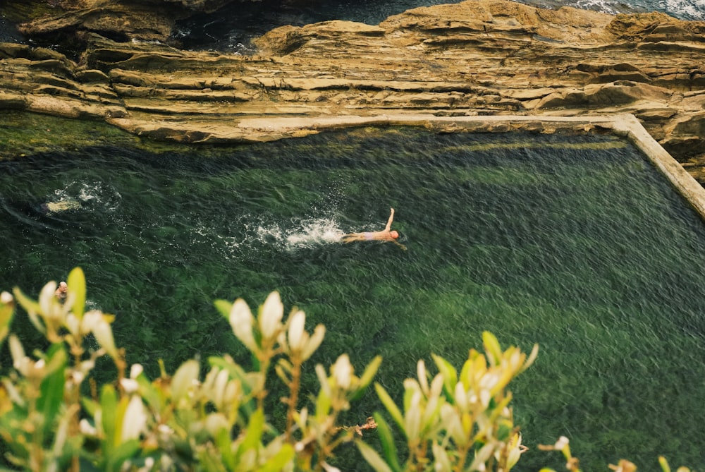 person swimming near brown cliff