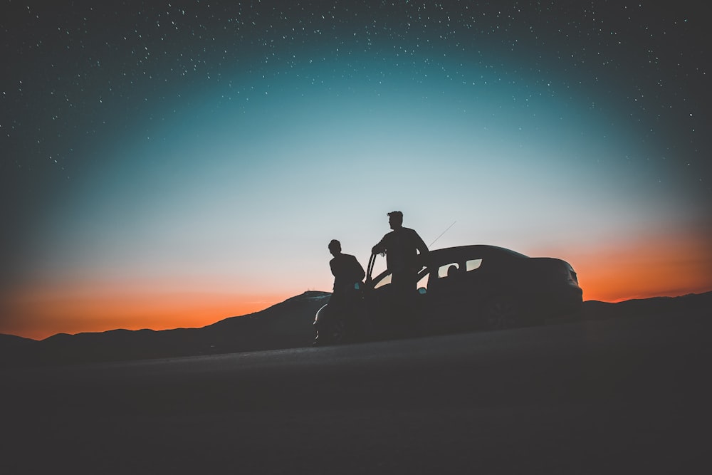 silhouette of two men beside car