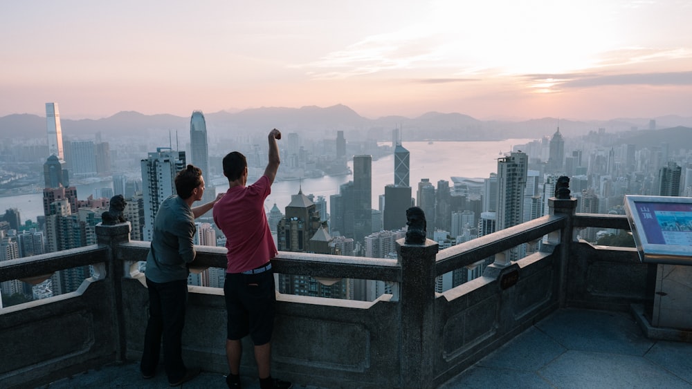 two men standing on top of building pointing to city at daytime