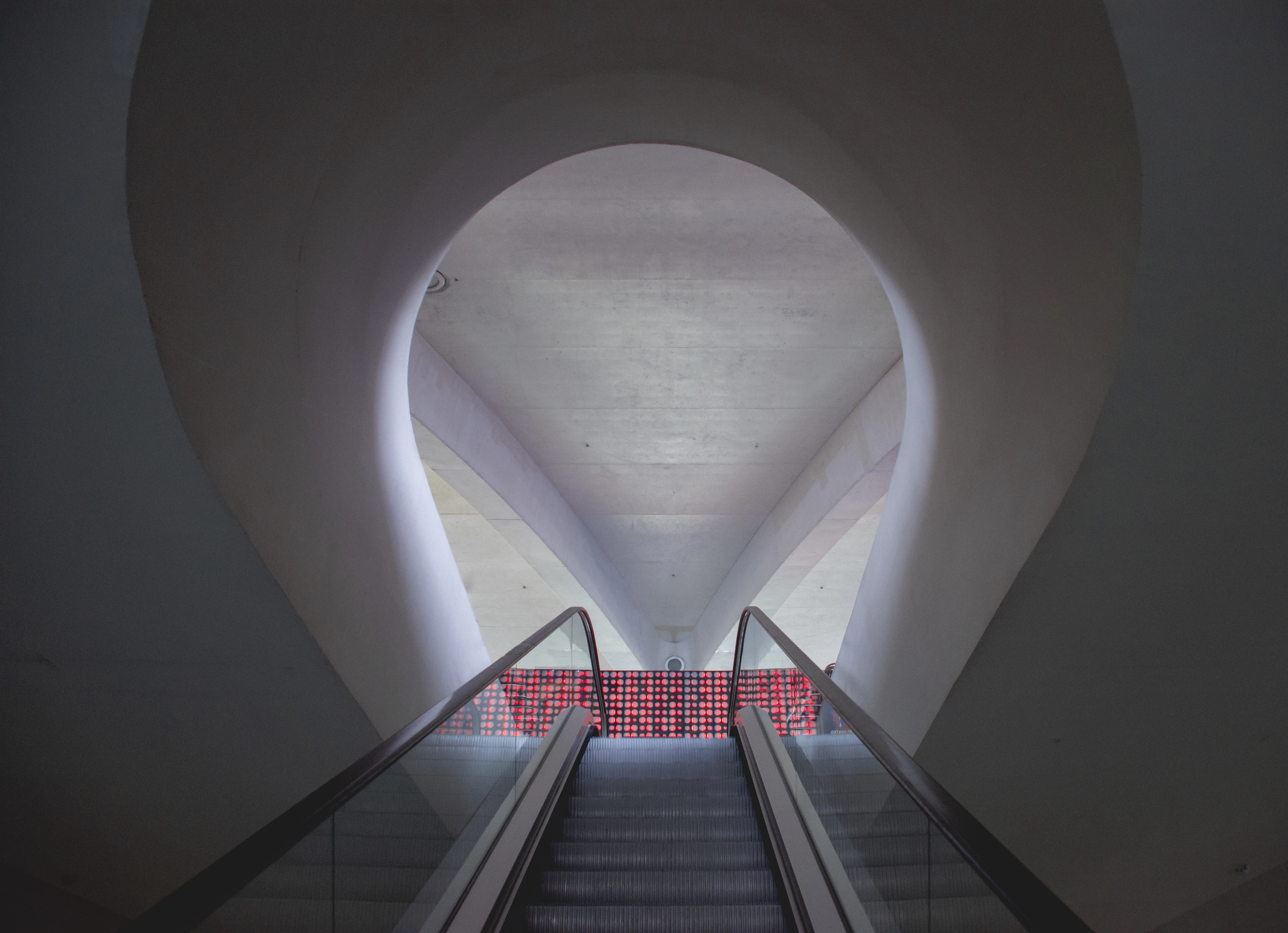 A red-lit escalator rises through a curved white concrete archway inside Valencia's City of Arts and Sciences.