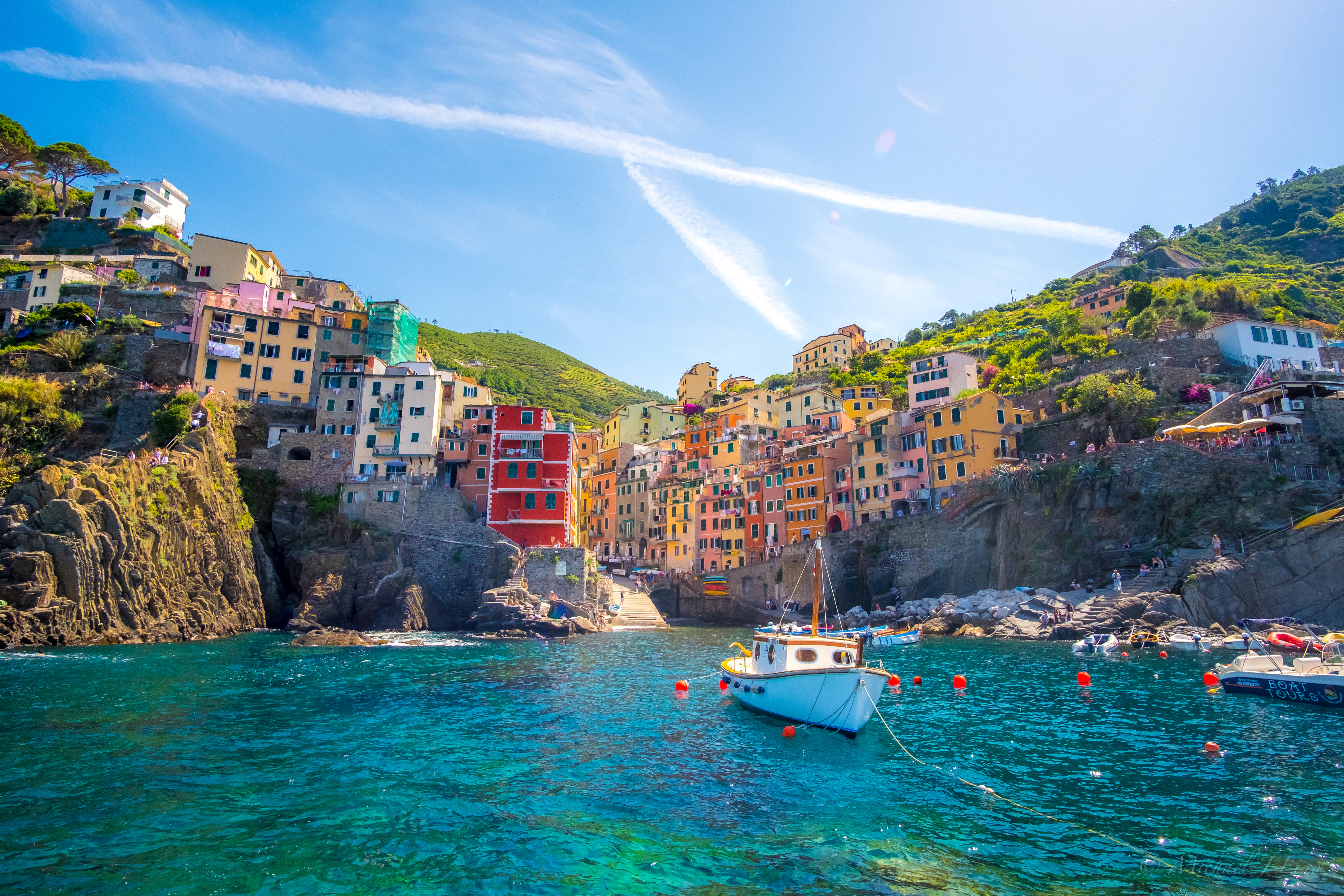 A Cinque Terre cove with pastel houses stacked on the cliff and a sailing boat anchored in clear water