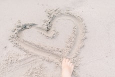 person forming heart on sand using right foot