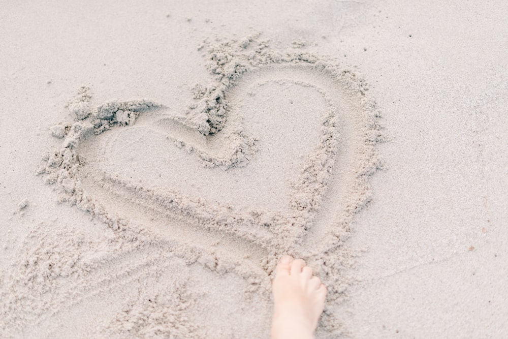 person forming heart on sand using right foot
