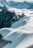A group of mountaineers is trekking across a snowy ridge, surrounded by towering jagged peaks and fluffy white clouds. The light casts long shadows, adding depth to the pristine, untouched snow.