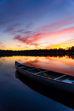 A serene northern lake at sunset with a lone canoe resting on the shore.