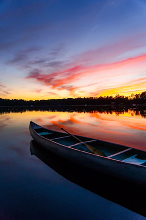 A serene mountain lake reflecting the golden hues of a sunset with a lone canoe drifting.