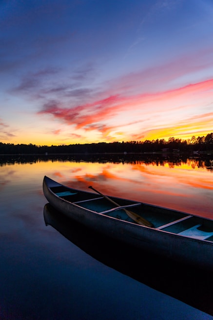 A vibrant sunset over a serene Banff lake, with a kayak resting on the shore ready for a paddle.