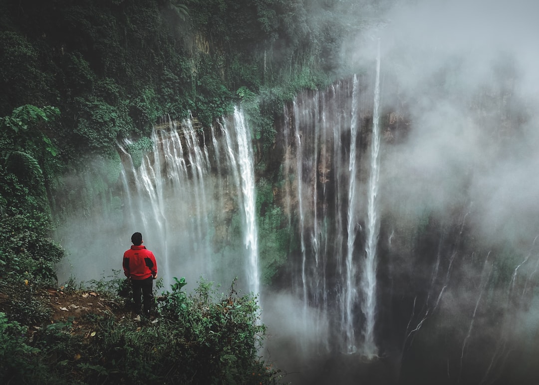 man standing on cliff facing waterfall