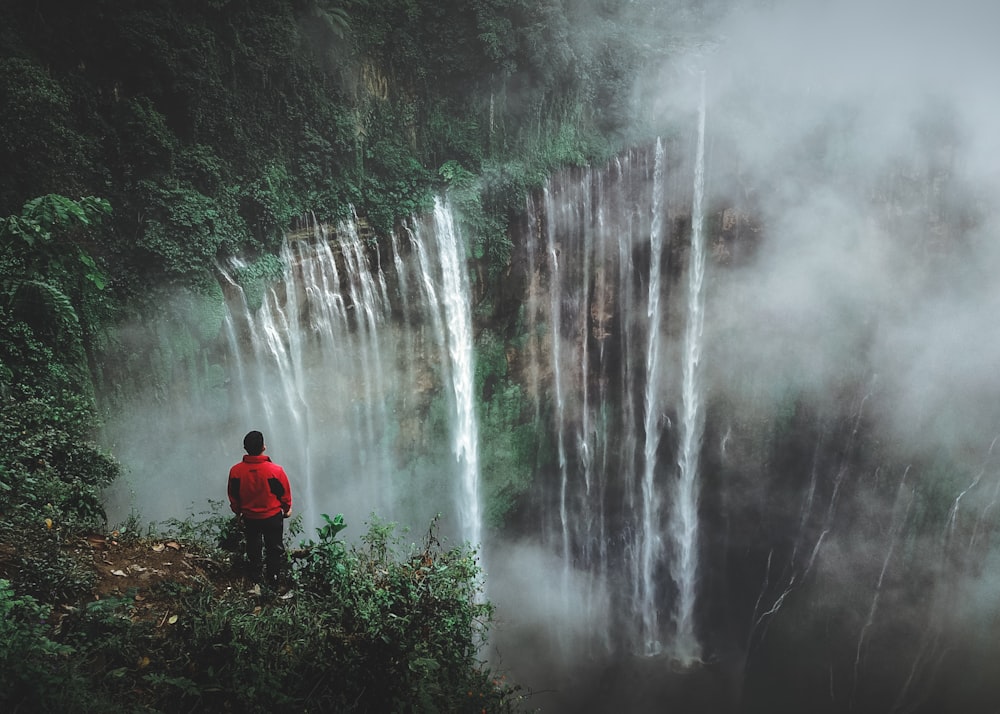 man standing on cliff facing waterfall