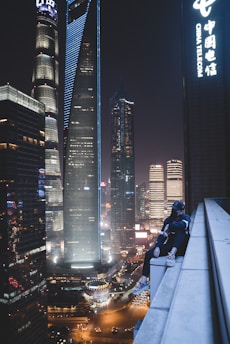 man sitting on building gutter during nighttime