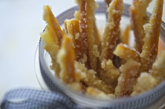 A close-up of candied orange peels coated in sugar and arranged in a glass jar, with a decorative ribbon tied around it.