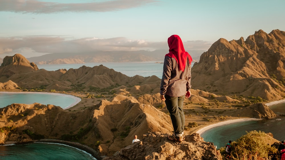 Persona de pie en un acantilado rodeado de montañas rocosas marrones y cuerpo de agua