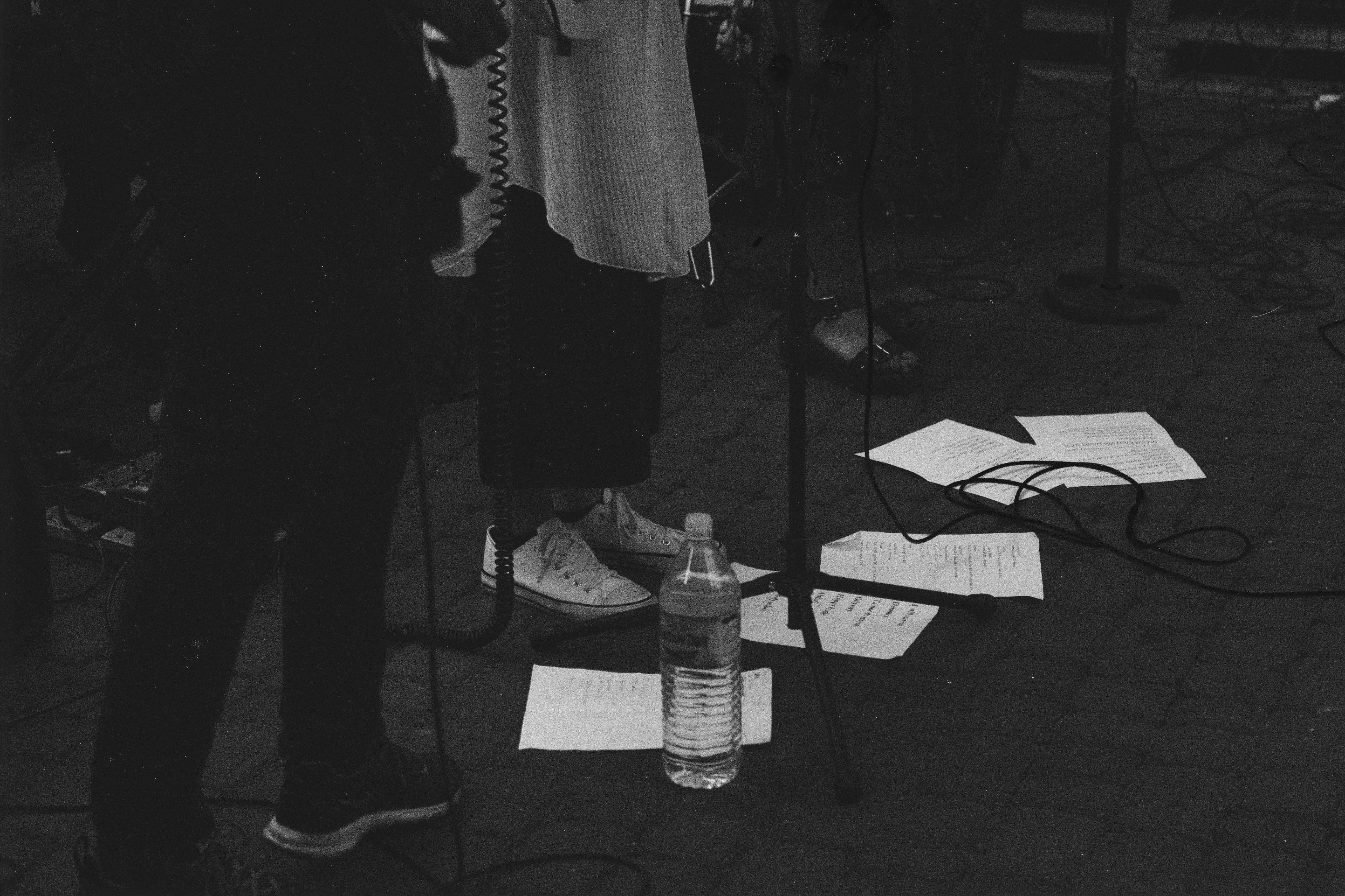 Foto en escala de grises de los pies de tres personas de pie cerca de los soportes del micrófono